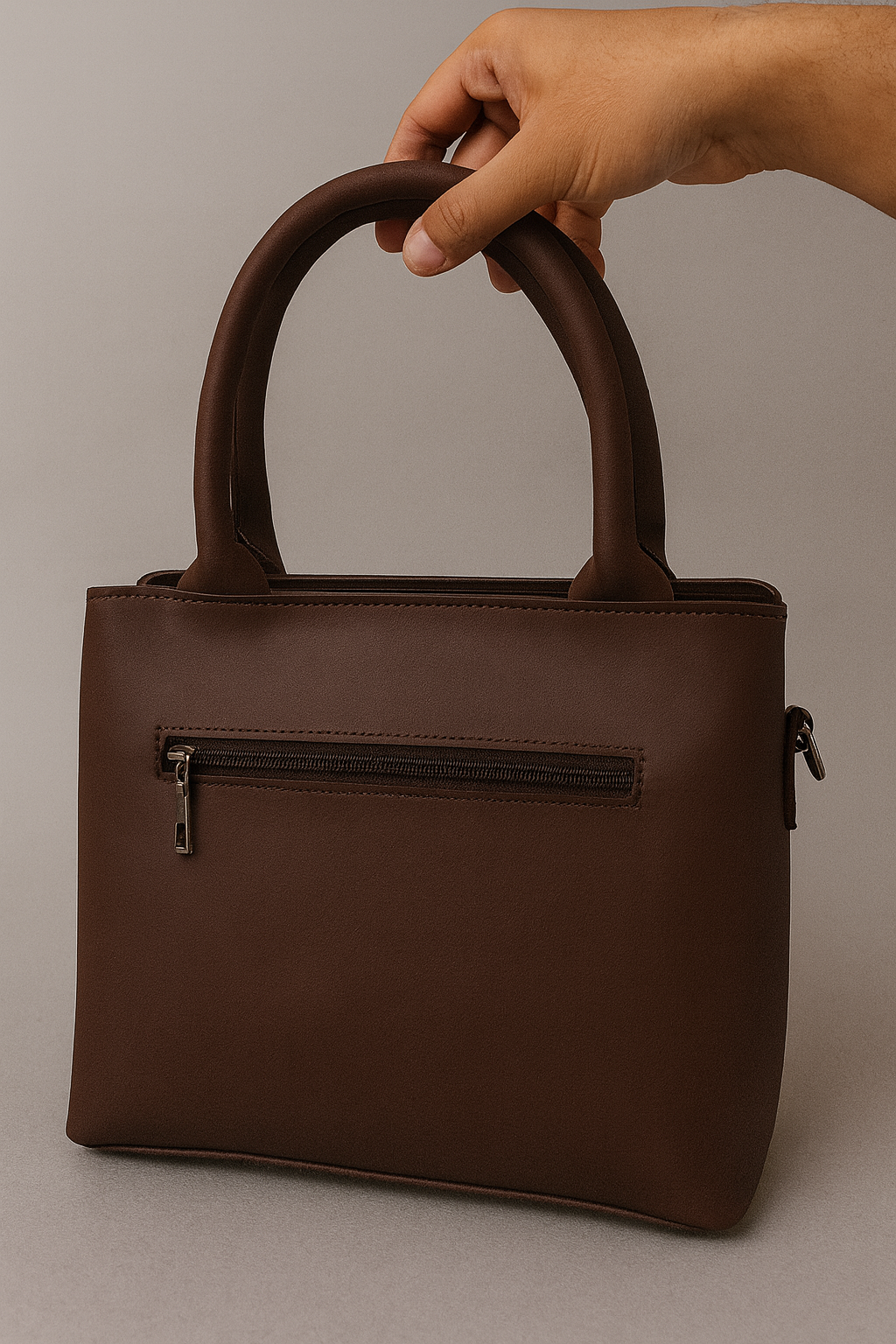 Brown handbag held by a hand against a neutral background