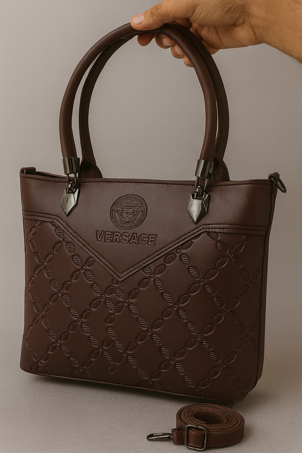 Brown Versace handbag held by a hand on a neutral background