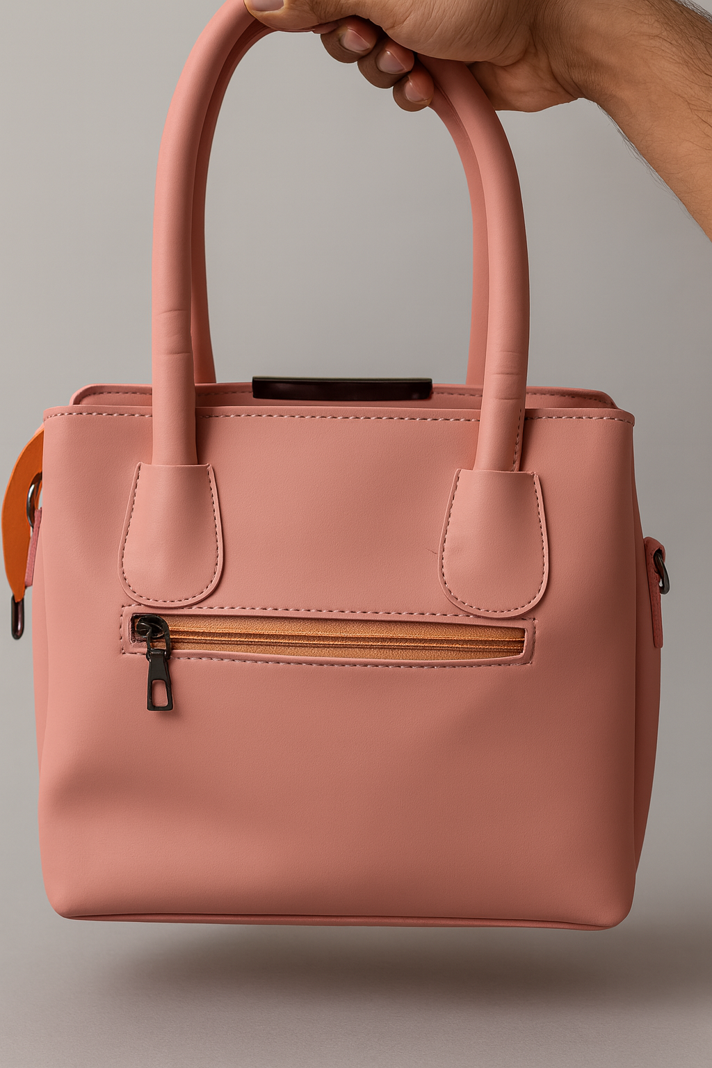 Pink handbag held by a hand against a neutral background