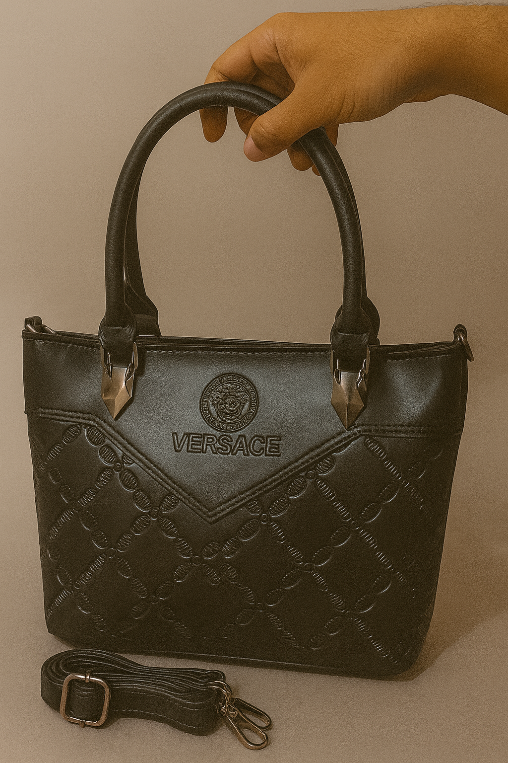 Black Versace handbag held by a hand against a beige background