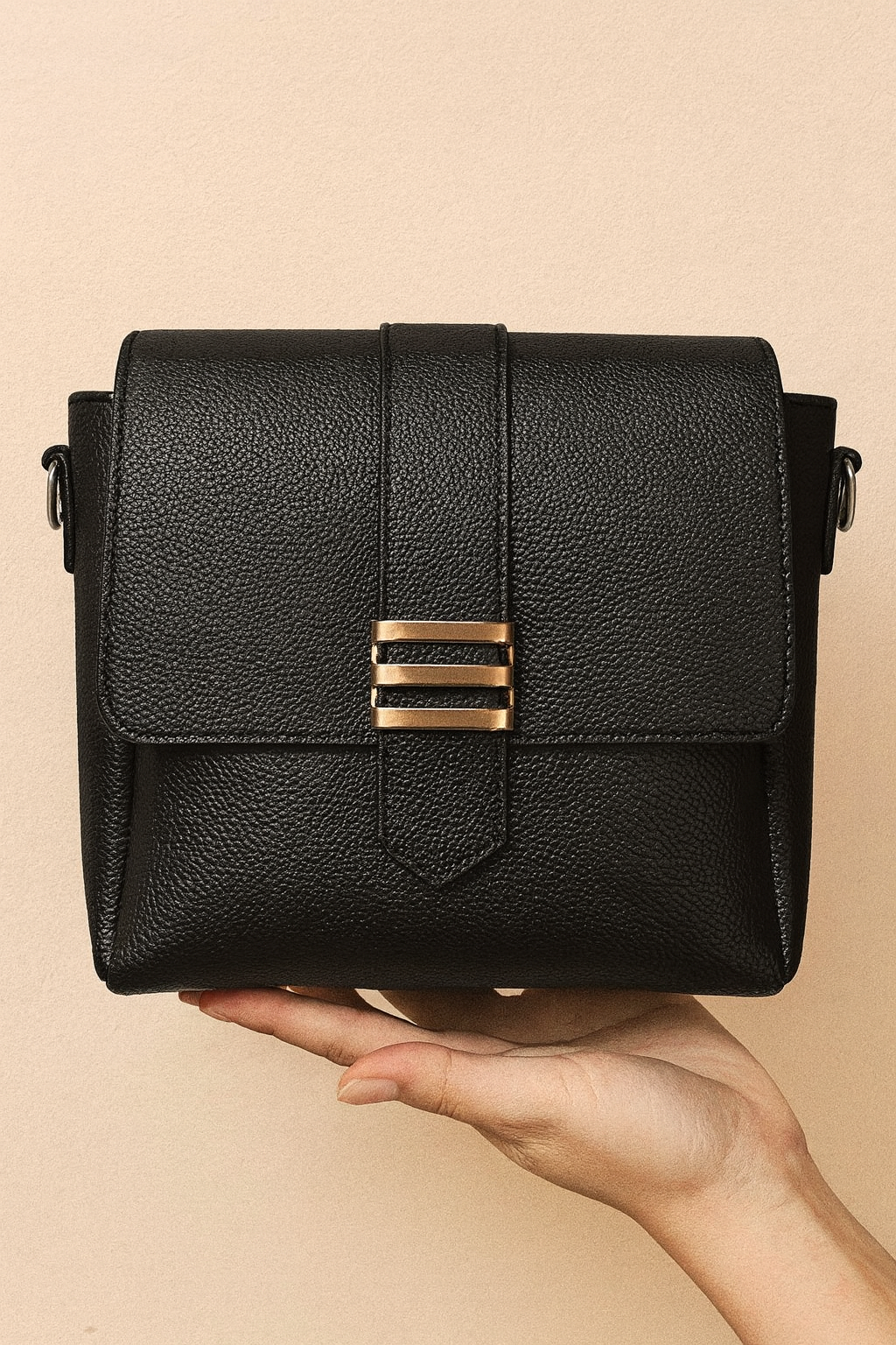 Black leather handbag with gold accents held in a hand against a beige background