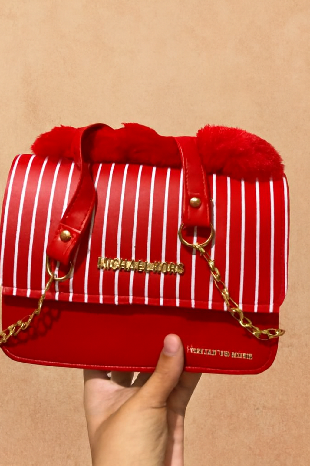 Red striped handbag with fur accents held by a hand against a beige background