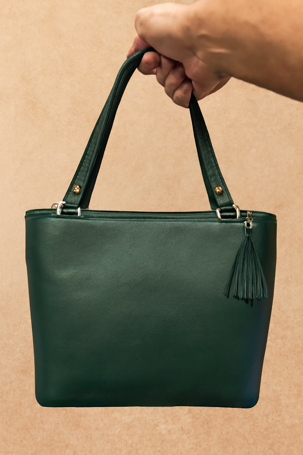 Green handbag with a tassel held by a hand on a beige background