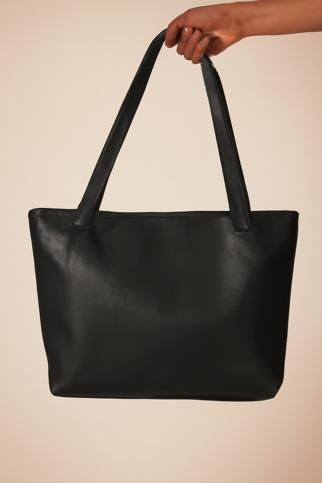 Black leather tote bag held by a hand against a beige background