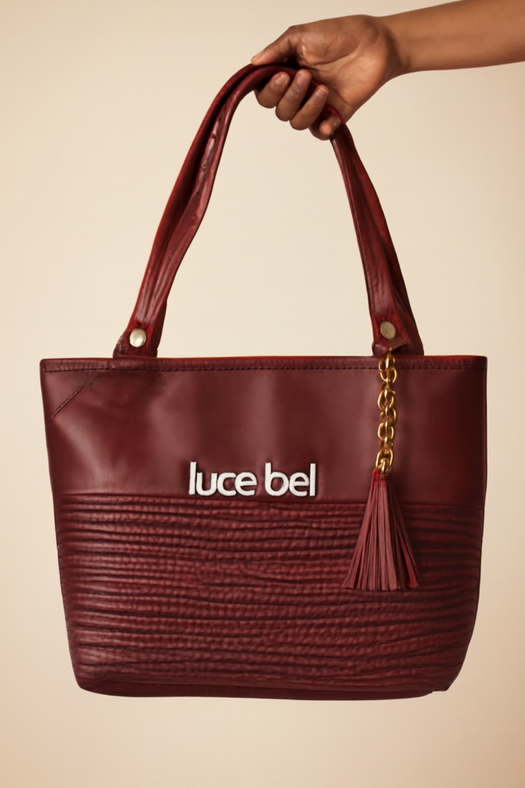 Maroon handbag with 'luce bel' branding held by a hand against a beige background