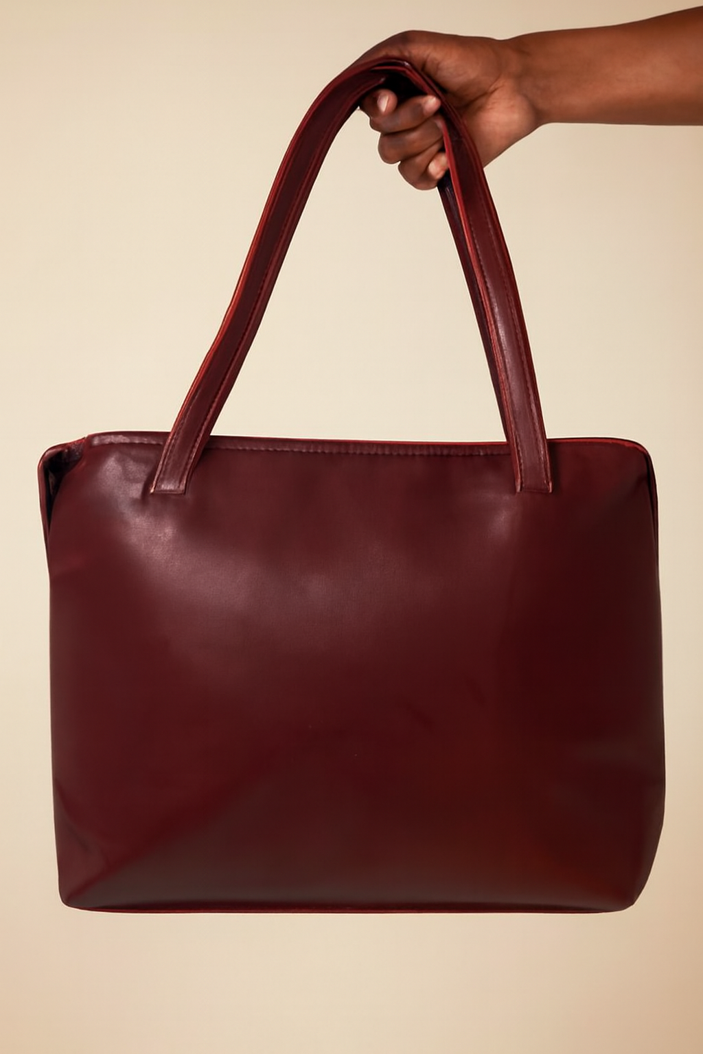 Brown leather handbag held by a hand against a beige background