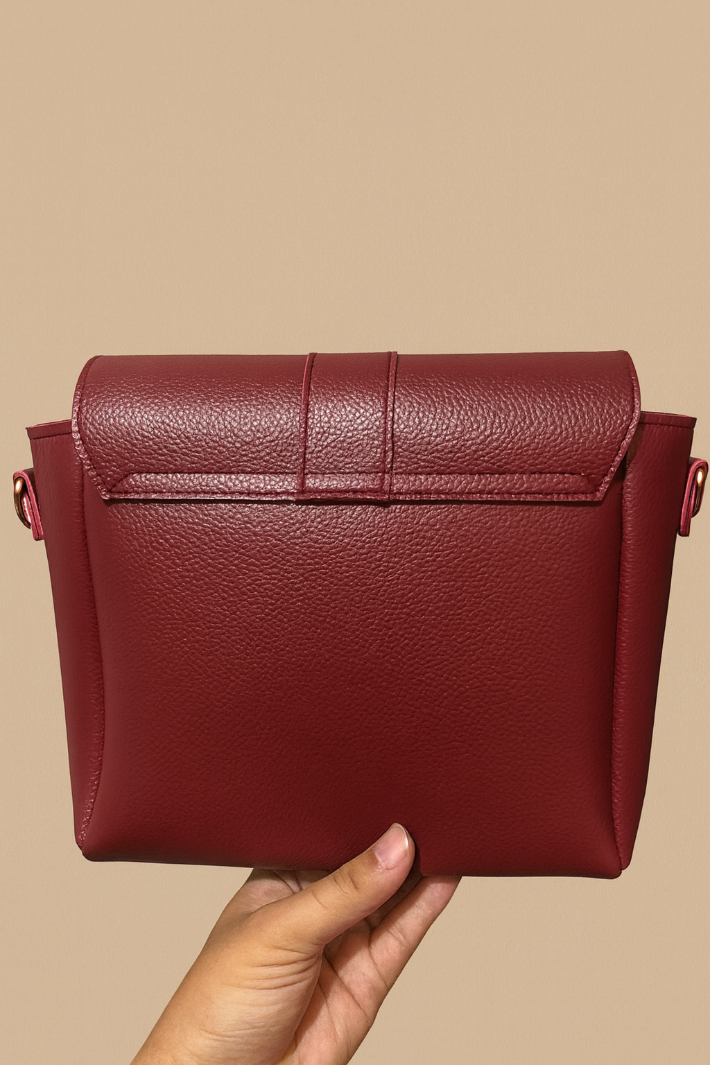 Red leather handbag held by a hand against a beige background