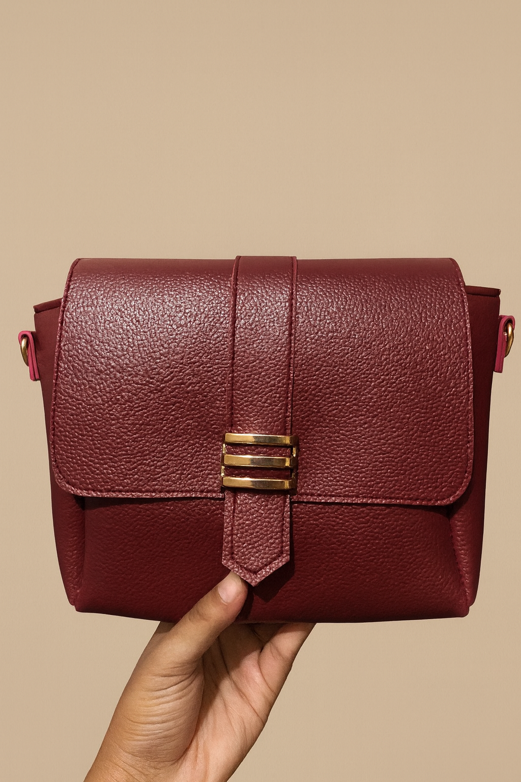 Red handbag with gold clasp held by a hand against a beige background