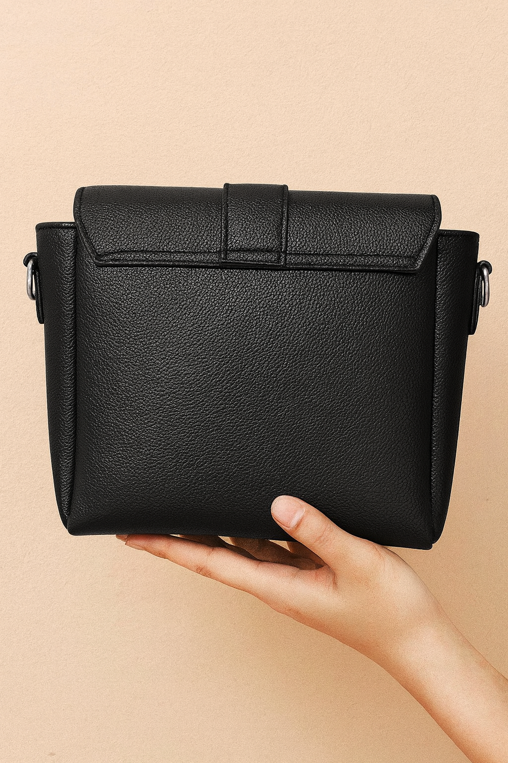 Black leather handbag held by a hand against a beige background