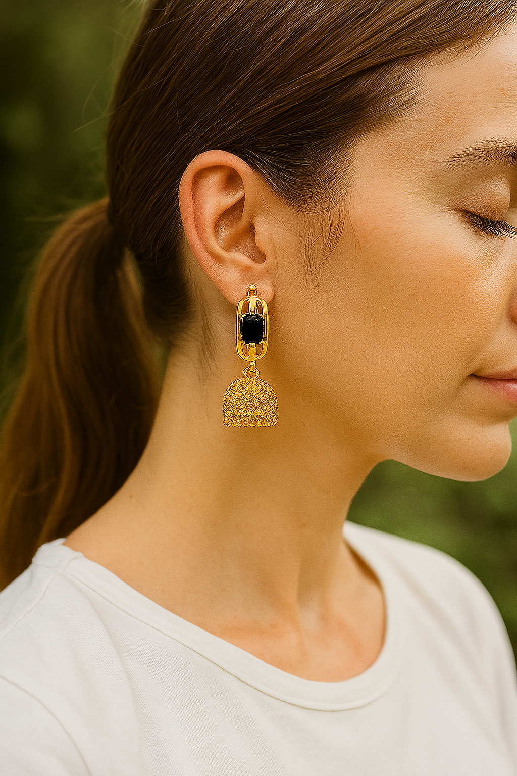 Close-up of a woman wearing gold earrings with a dark gemstone against a blurred green background