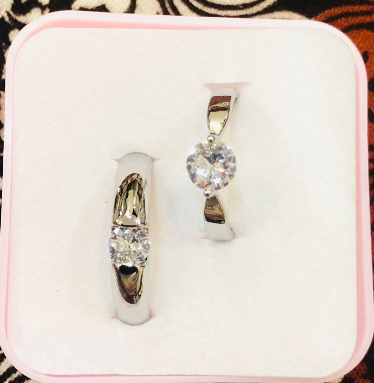 Gold hoop earrings with clear gemstones on a pink cushioned stand.