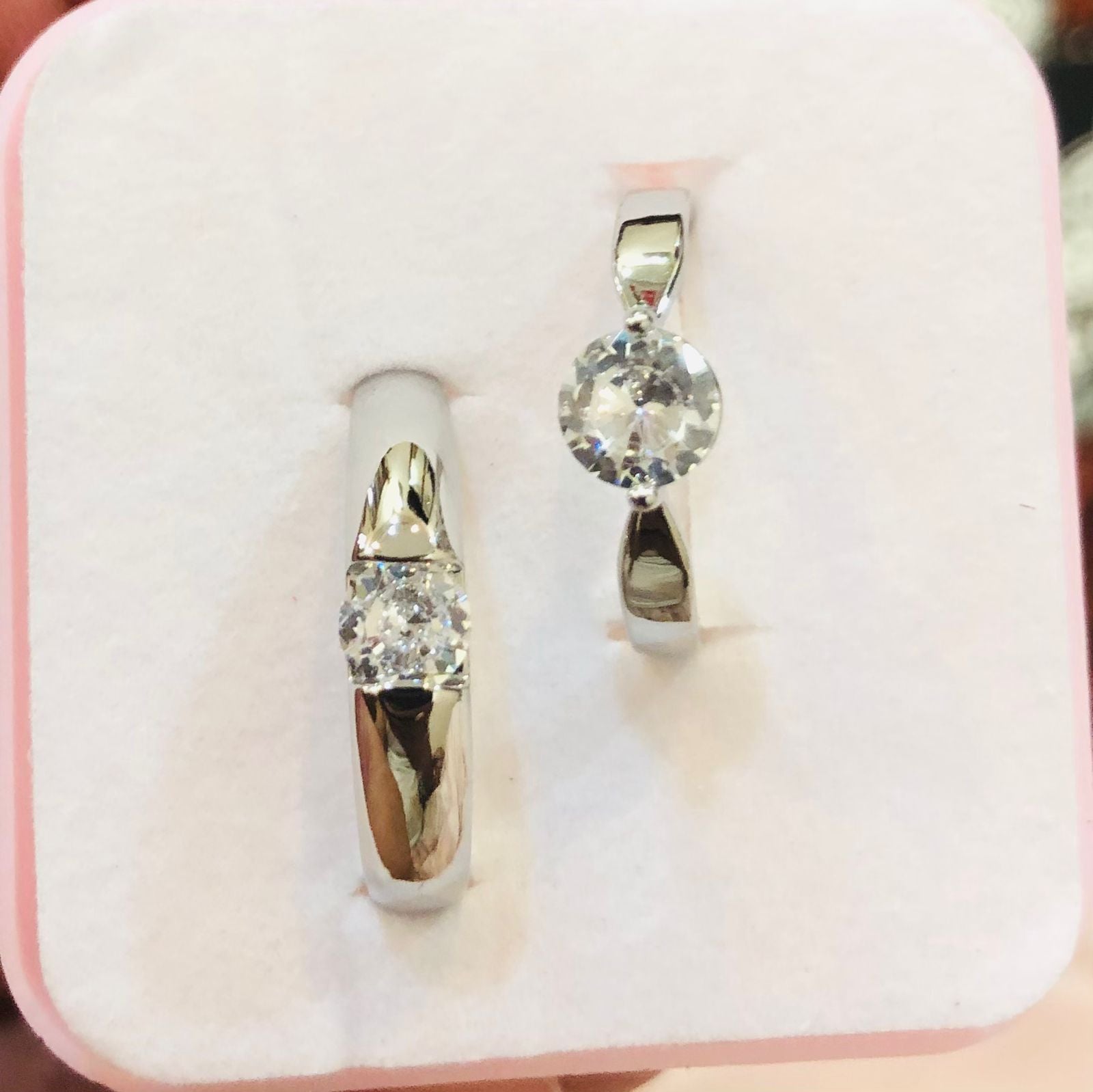 Pair of silver earrings with clear gemstones on a pink jewelry box.