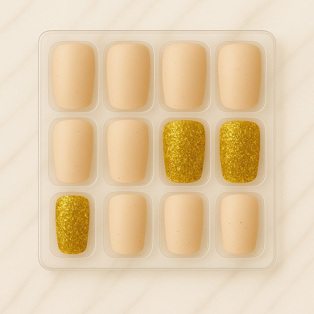 Set of beige and gold glitter nail art pieces in a clear plastic tray on a beige background